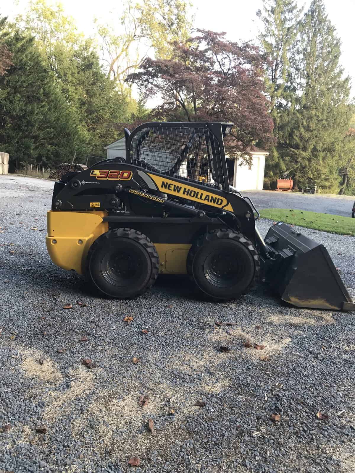 IMG_0741 (1) New Holland L320 skid steer loader with bucket attachment on gravel surface.