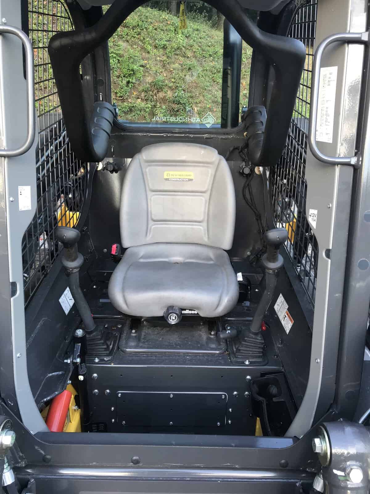 IMG_0744 (1) Operator seat inside a compact construction equipment cab with safety bars and controls.