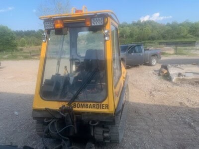 Yellow Bombardier compact utility vehicle with enclosed cab and tracks on a construction site.