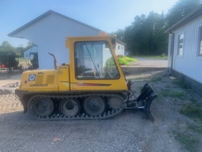 Yellow Bomag Bomardier multi-track loader with blade attachment on gravel surface.