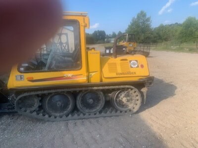 Yellow Bomag BW120AD-4 compact track loader with enclosed cab and rubber tracks on a construction site.