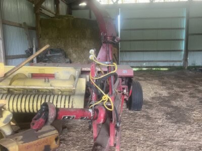 New Holland 782 forage harvester attachment inside barn with metal roof and dirt floor.