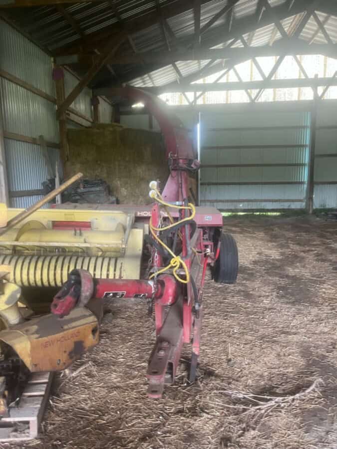 New Holland 782 forage harvester attachment inside barn with metal roof and dirt floor.