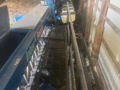 Blue and black agricultural machinery with tracks and attachments in storage shed.