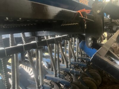 John Deere 1775NT planter with multiple row units and hydraulic components under a barn roof.