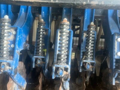 Close-up of blue tillage equipment with spring-loaded tines and soil contact points.