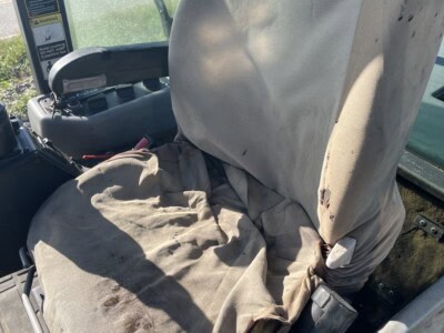 Worn construction equipment seat with fabric tear and dirt, suitable for heavy machinery like excavators or loaders.