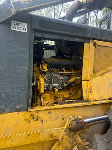 IMG_4590 Yellow construction equipment engine compartment with visible hydraulic components and caution sign.