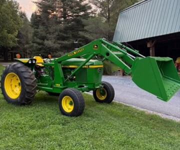 Green John Deere 2440 compact tractor with front loader and yellow wheels on grassy area.
