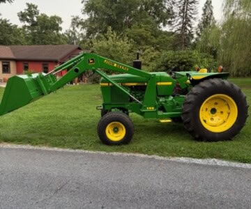 John Deere 2440 compact utility tractor with front loader and rear hitch, green and yellow color scheme, in a grassy area.