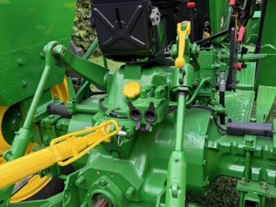 Green John Deere 2440 tractor with yellow accents and attached implements, detailed view of engine and controls.