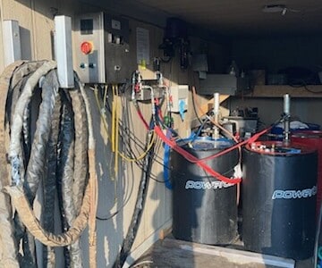 Electrical control panels, hoses, and tanks for spray foam insulation system in workshop.