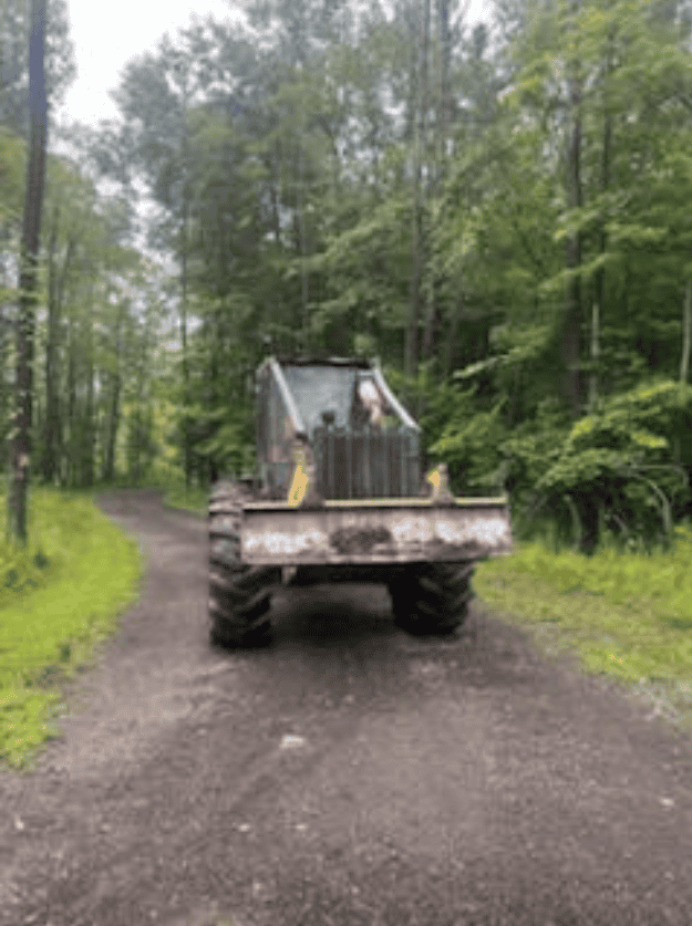 Screenshot 2026-09-09 113554 Front view of a large Caterpillar bulldozer on a dirt trail in a forested area.