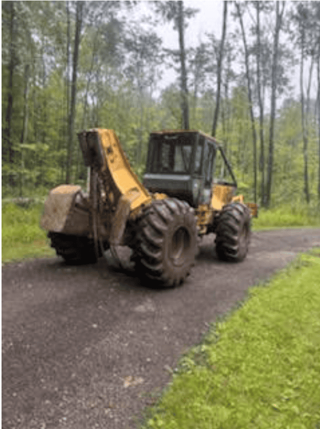 Screenshot 2026-09-09 113559 Yellow John Deere backhoe loader on a gravel path in a wooded area.