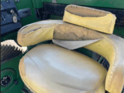 Worn yellow tractor seat with torn padding and visible foam inside, green interior background.
