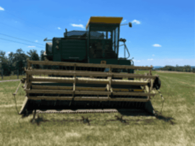 John Deere 6600 combine harvester with yellow cab and cutting header in a field under blue sky.