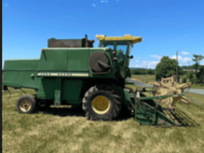 John Deere 6600 combine harvester with yellow cab and cutting header on grassy field.