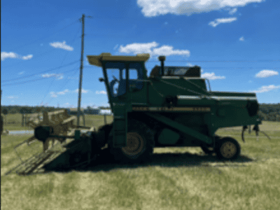 Green John Deere 6600 tractor with mowing attachment on a grassy field under blue sky.