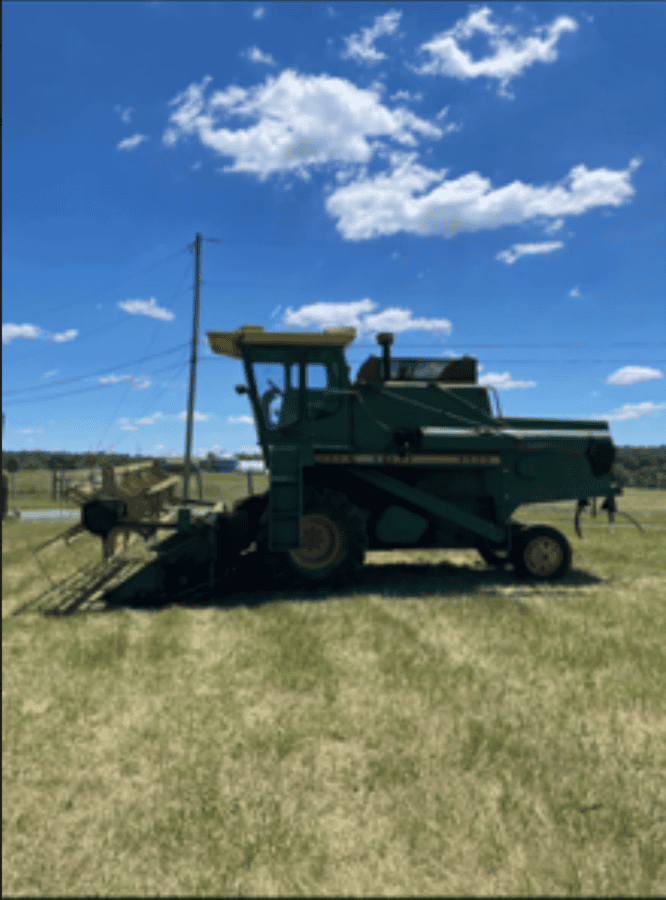 Green John Deere 6600 tractor with mowing attachment on a grassy field under blue sky.