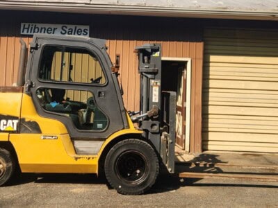 Yellow Caterpillar forklift with black tires parked outside Hibner Sales building.