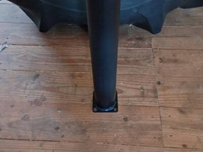 Black support leg attached to a yellow and black industrial tank on wooden floor.
