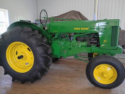 John Deere 70 tractor with green body and yellow wheels inside a barn.