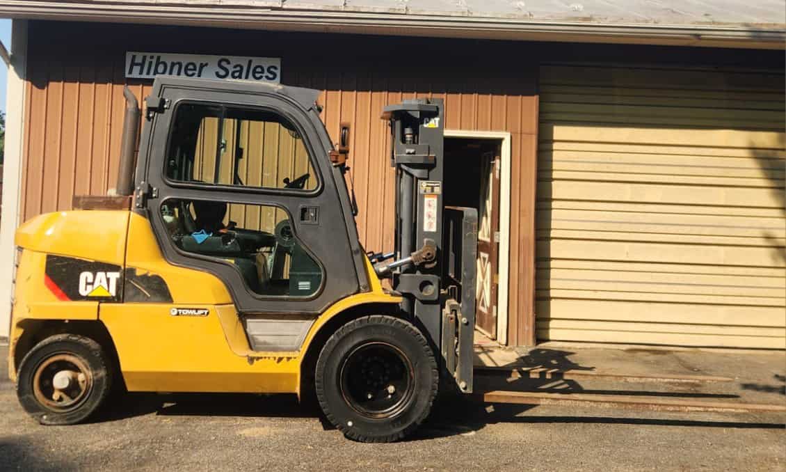 Yellow Caterpillar forklift with black tires parked outside Hibner Sales building.