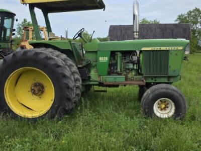 Green John Deere 4620 tractor with canopy and large rear tires on grassy field.
