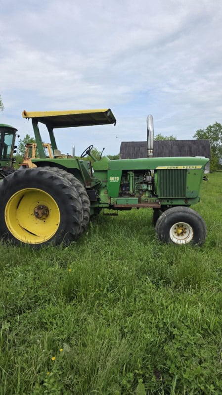Green John Deere 4620 tractor with canopy and large rear tires on grassy field.