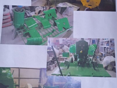 Green agricultural equipment with yellow safety helmet in workshop setting.