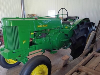 Green John Deere 70 tractor with black tires and yellow rims inside a barn.