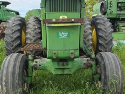 Green John Deere tractor with raised hood and large rear tires on grassy field.