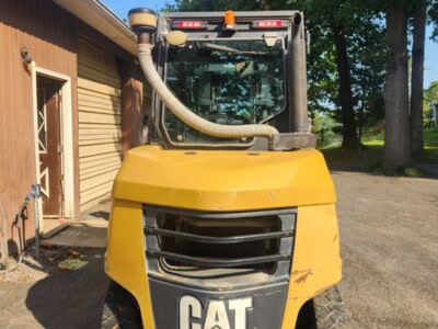 Yellow Caterpillar LPG forklift with black tires and cab, parked outside near trees and a building.