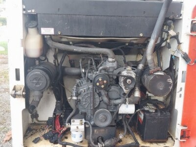 Front view of a compact construction equipment engine with visible belts and hoses.
