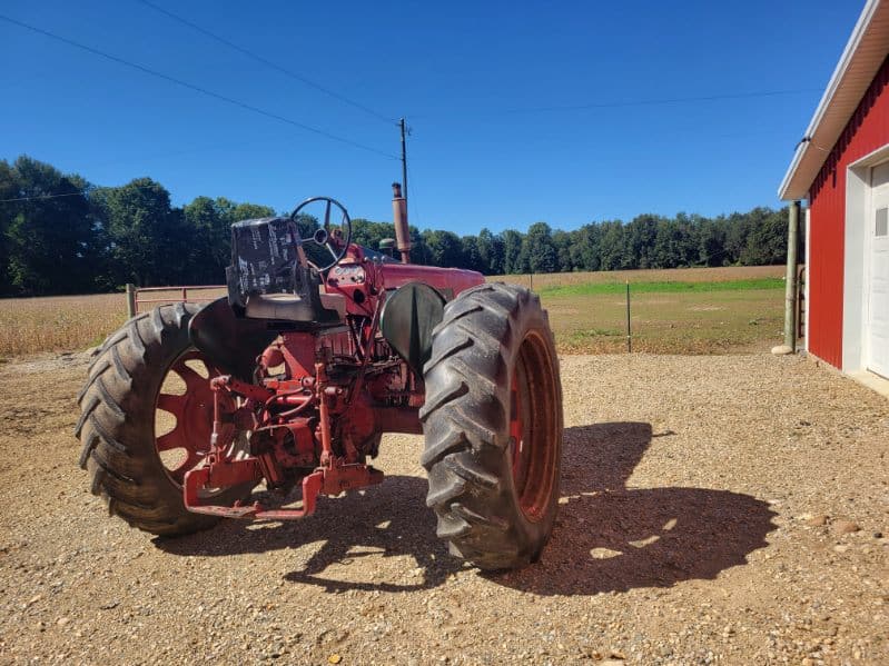 image000002 (8) Red Farmall 450 tractor with large rear tires and enclosed cab, parked on gravel near a barn.