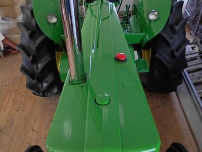 Green John Deere tractor with large rear tires and enclosed cab, front view.