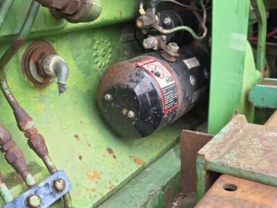 Close-up of a green John Deere tractor engine with visible hydraulic components and wiring.