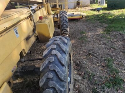Yellow construction equipment with large tires and a raised platform in a backyard setting.