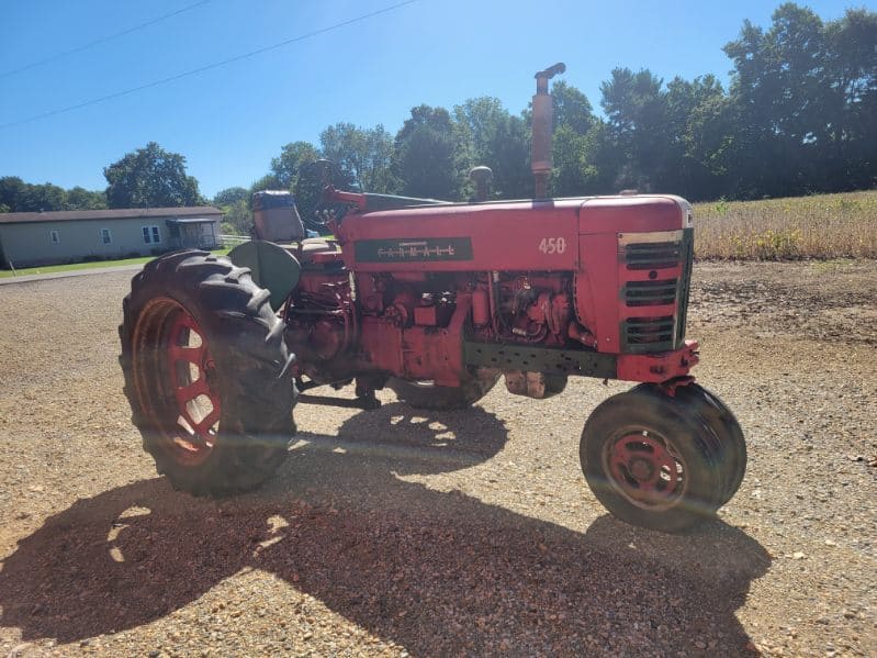 Red Farmall 450 tractor with large rear tires and smaller front tires on gravel surface.
