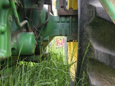 Close-up of tractor wheel and undercarriage with grass in foreground.