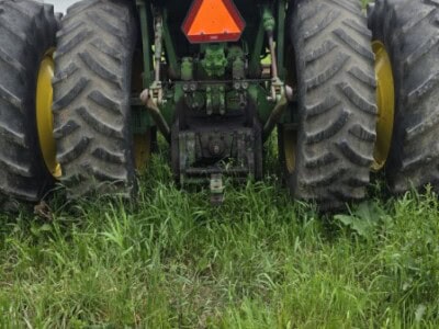 Green John Deere tractor with large rear tires and a canopy, parked on grass.