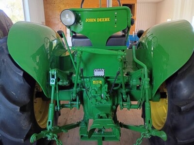 John Deere tractor with green body and large rear tires, front view showing engine and steering components.