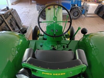 John Deere green tractor with black seat and steering wheel, front view, indoor setting.