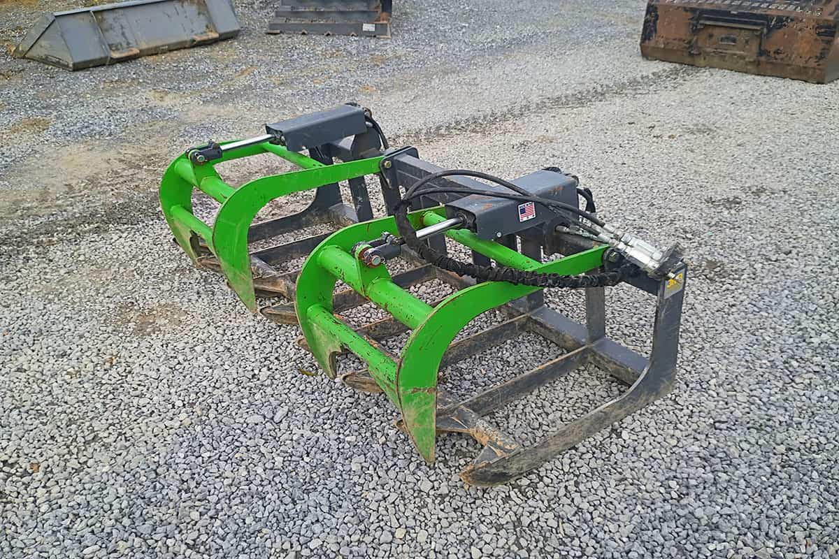 Heavy-duty grapple attachment for skid steer loaders Green and black skid steer grapple attachment with hydraulic cylinders on gravel surface.
