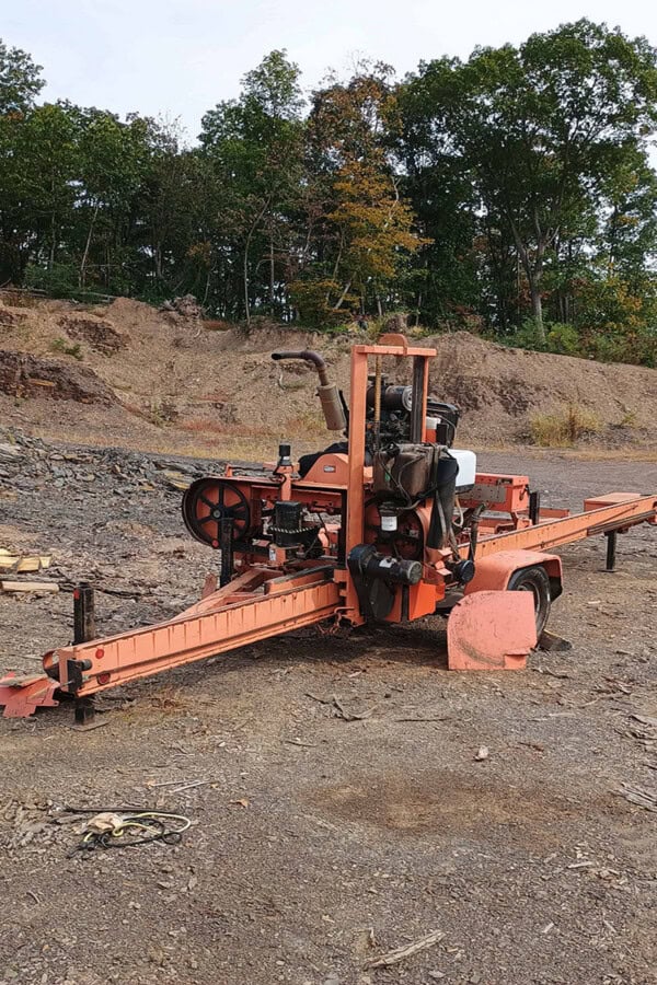 Wood-Mizer LT40 hydraulic sawmill with orange frame and cutting bed on uneven ground.