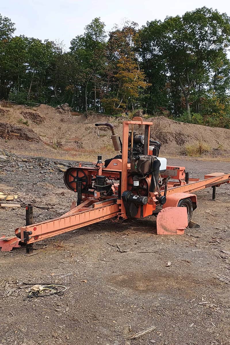 1000010691 (1) copy Wood-Mizer LT40 hydraulic sawmill with orange frame and cutting bed on uneven ground.