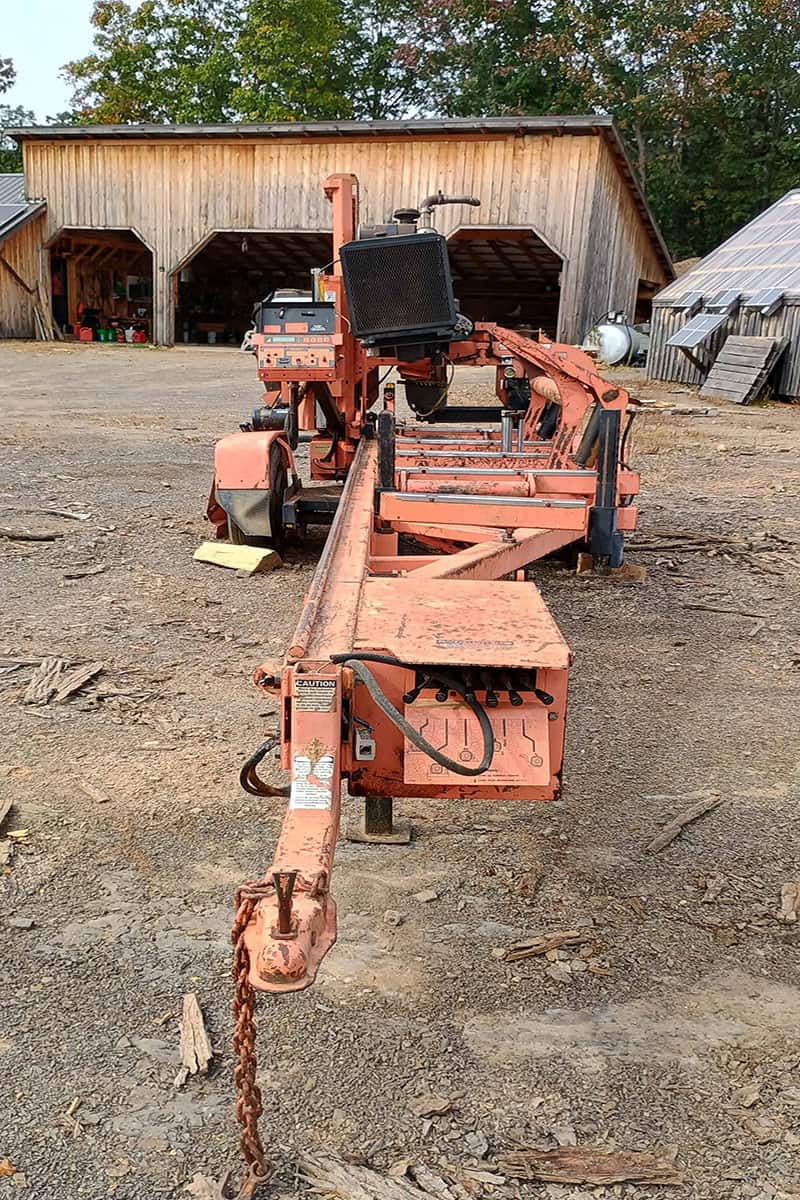 1000010693 (1) copy Orange industrial wood processing equipment with control panel and chain hitch on dirt ground.