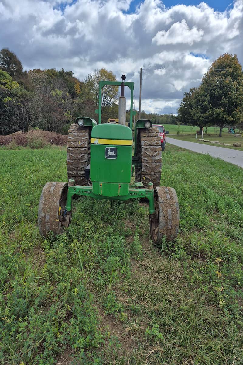 John Deere 5055E Tractor in Field Green John Deere 5055E tractor with large rear tires and enclosed cab in a grassy field.