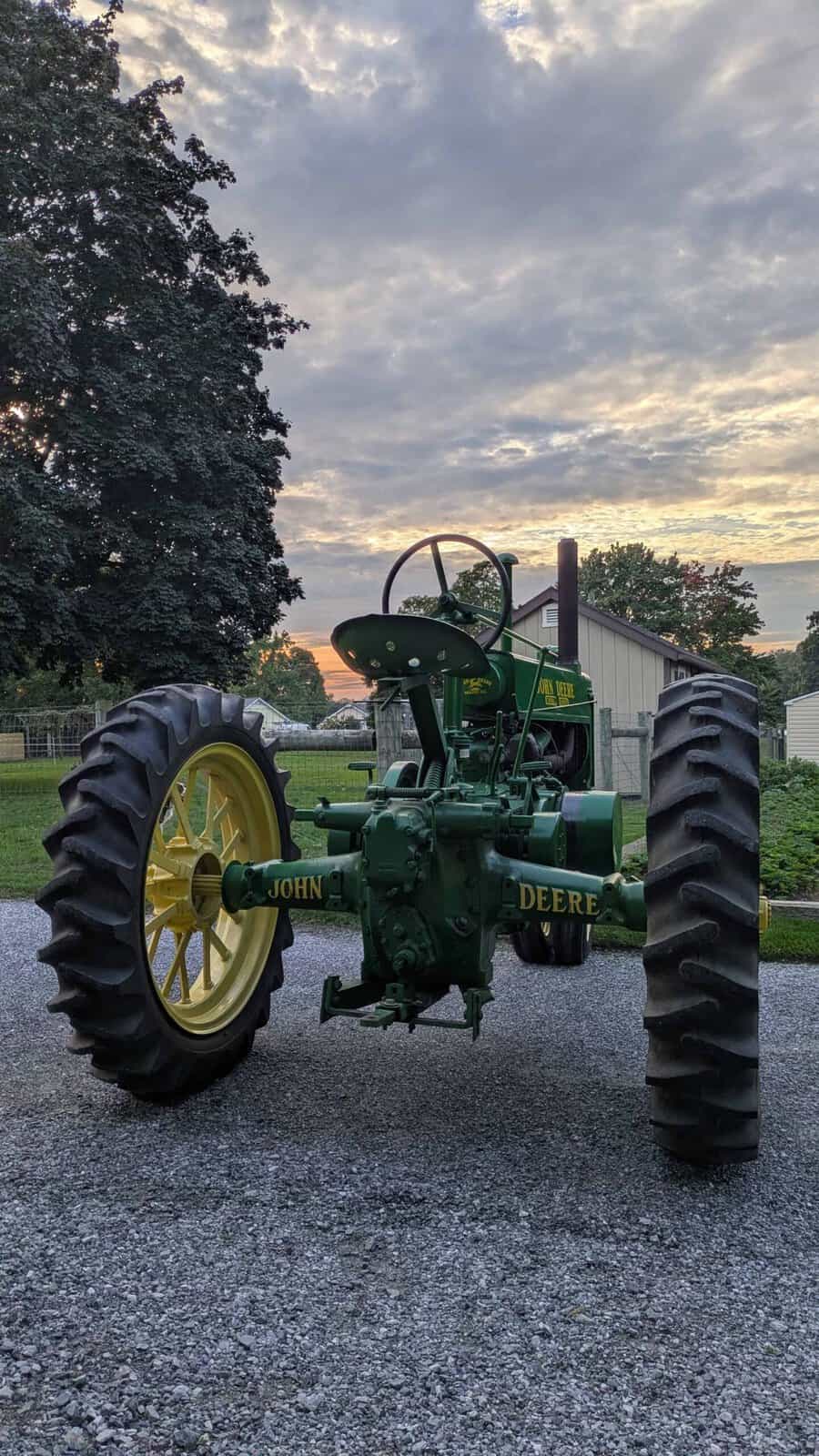 4450 (1) 1938 John Deere A tractor with large rear tires and steering wheel in an outdoor setting at sunset.