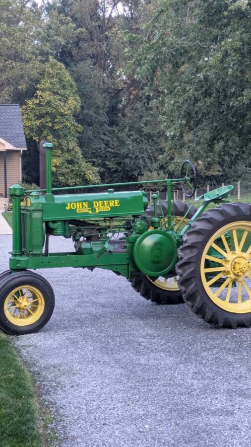 1938 John Deere A tractor with green body and yellow wheels on a gravel driveway.